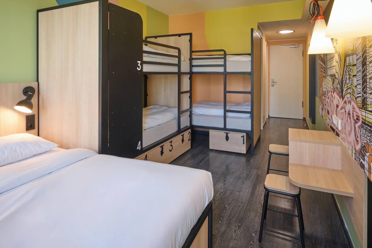 A dormitory room with bunk beds, a desk, and a chair.