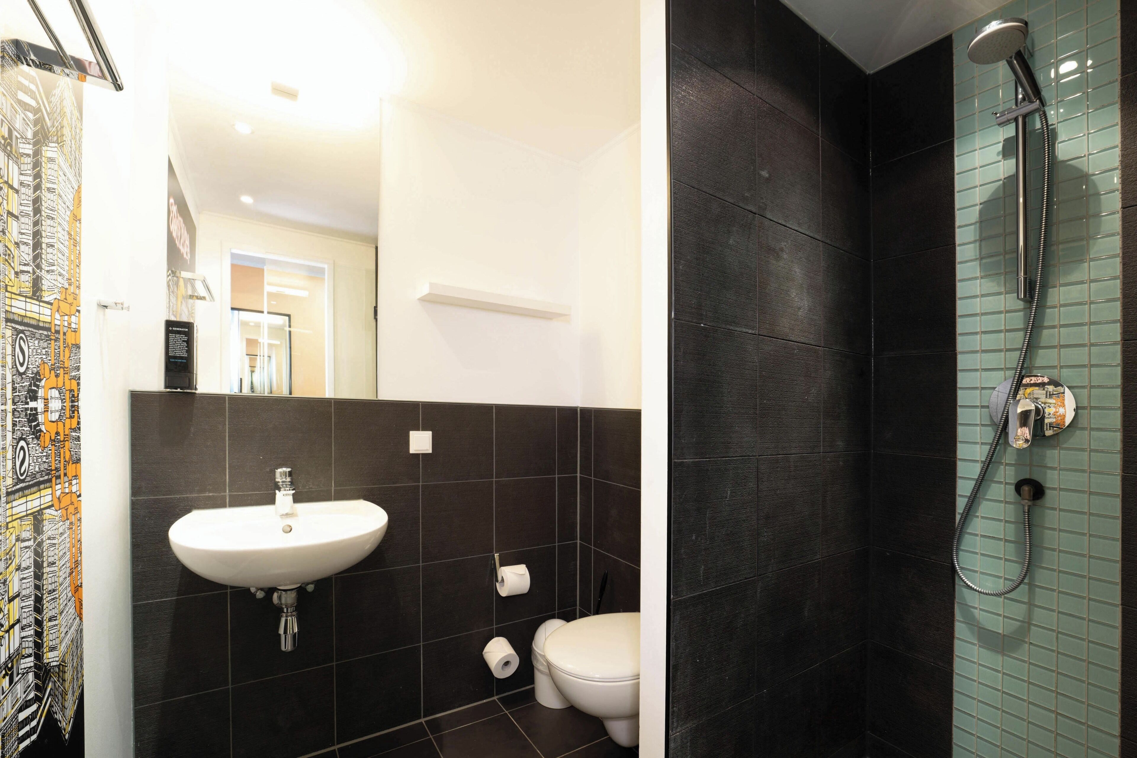 A bathroom with a white sink, dark tiled walls, a toilet, and a shower with a glass door.