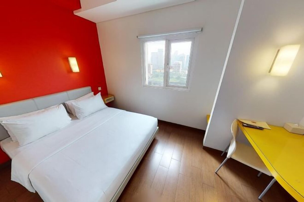 A hotel room with a bed, a window, a desk, and a chair.