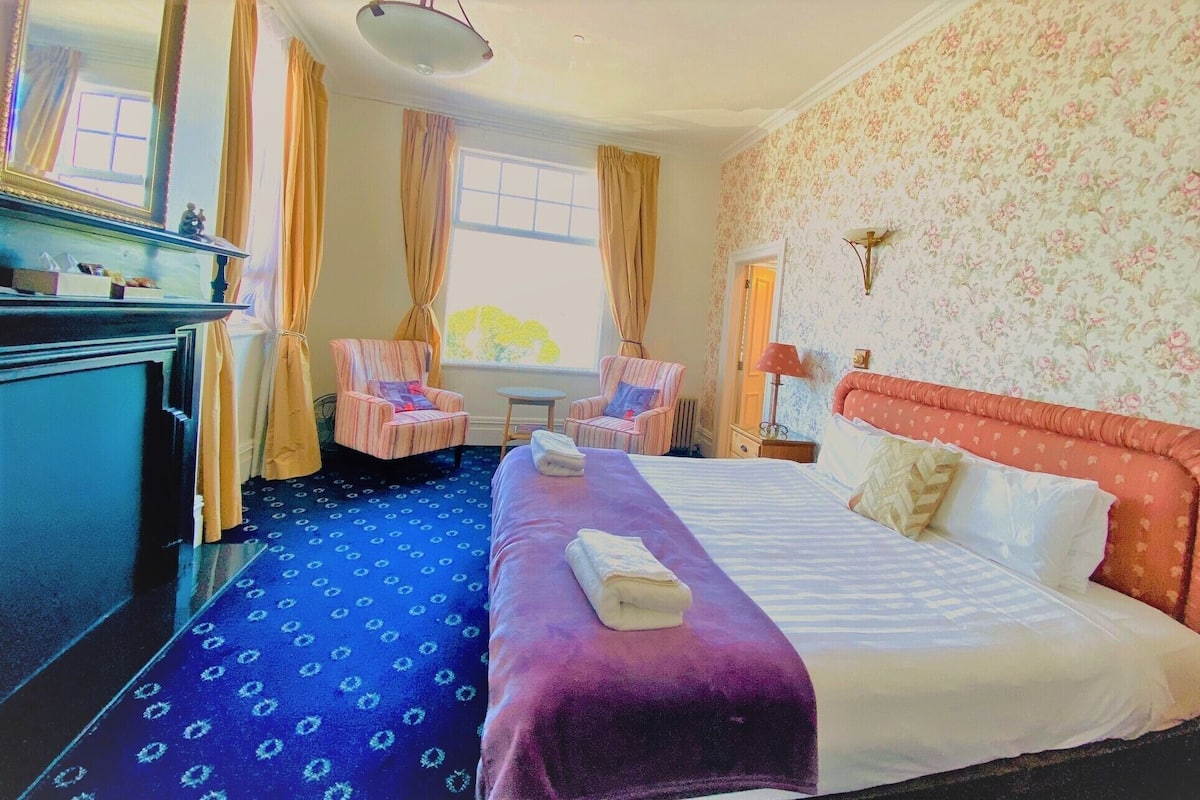 A hotel room with a large bed, two armchairs, a desk, and a dresser.