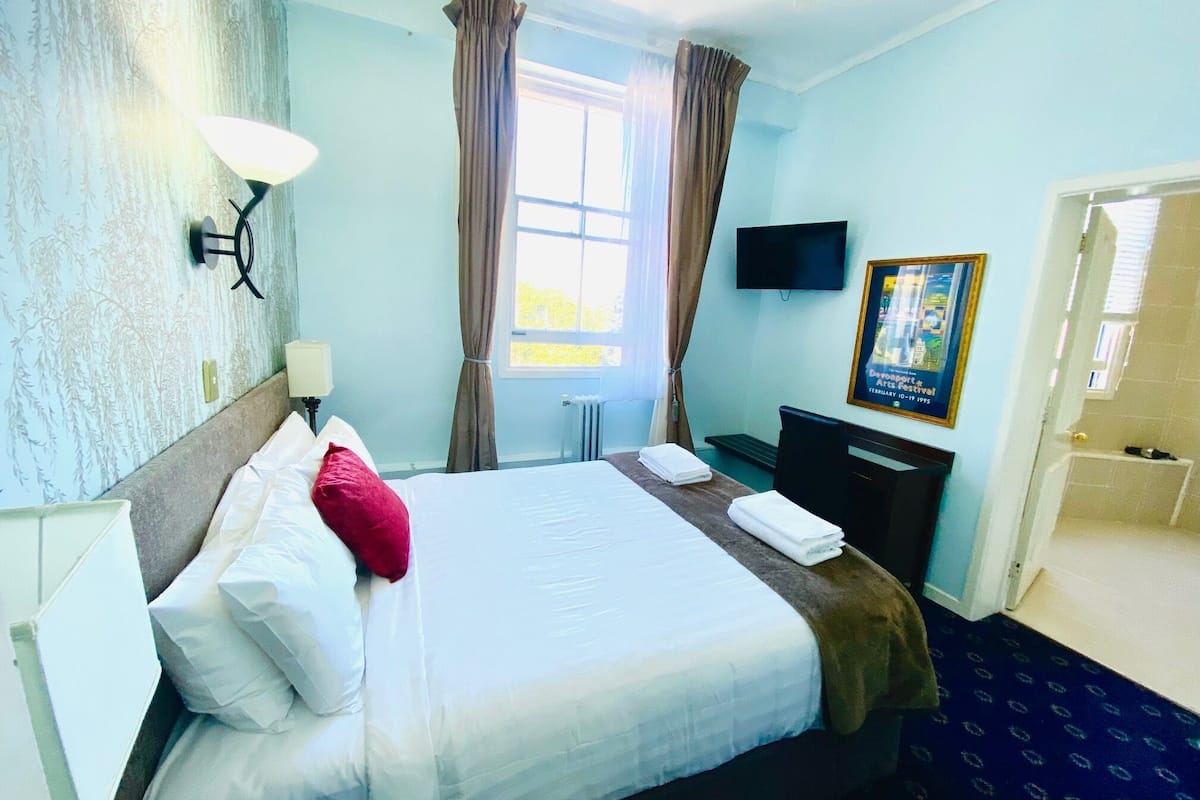 A hotel room with a bed, a desk, a chair, a TV, and a window with curtains.