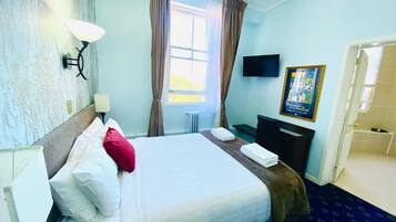 A hotel room with a bed, a desk, a chair, a TV, and a window with curtains.
