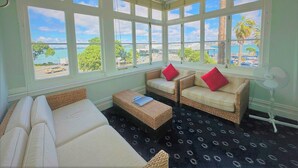 A sunlit room with a large bay window, wicker furniture, and a view of the sea. - The Esplanade Hotel (Auckland)