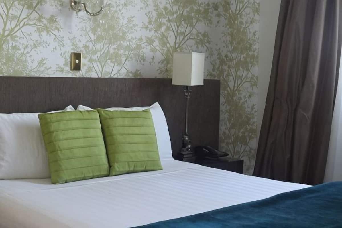 A hotel room with a bed, green pillows, a nightstand with a lamp, and a telephone.