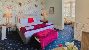 A hotel room with a bed, two bedside tables, a dresser, and a window with blinds.