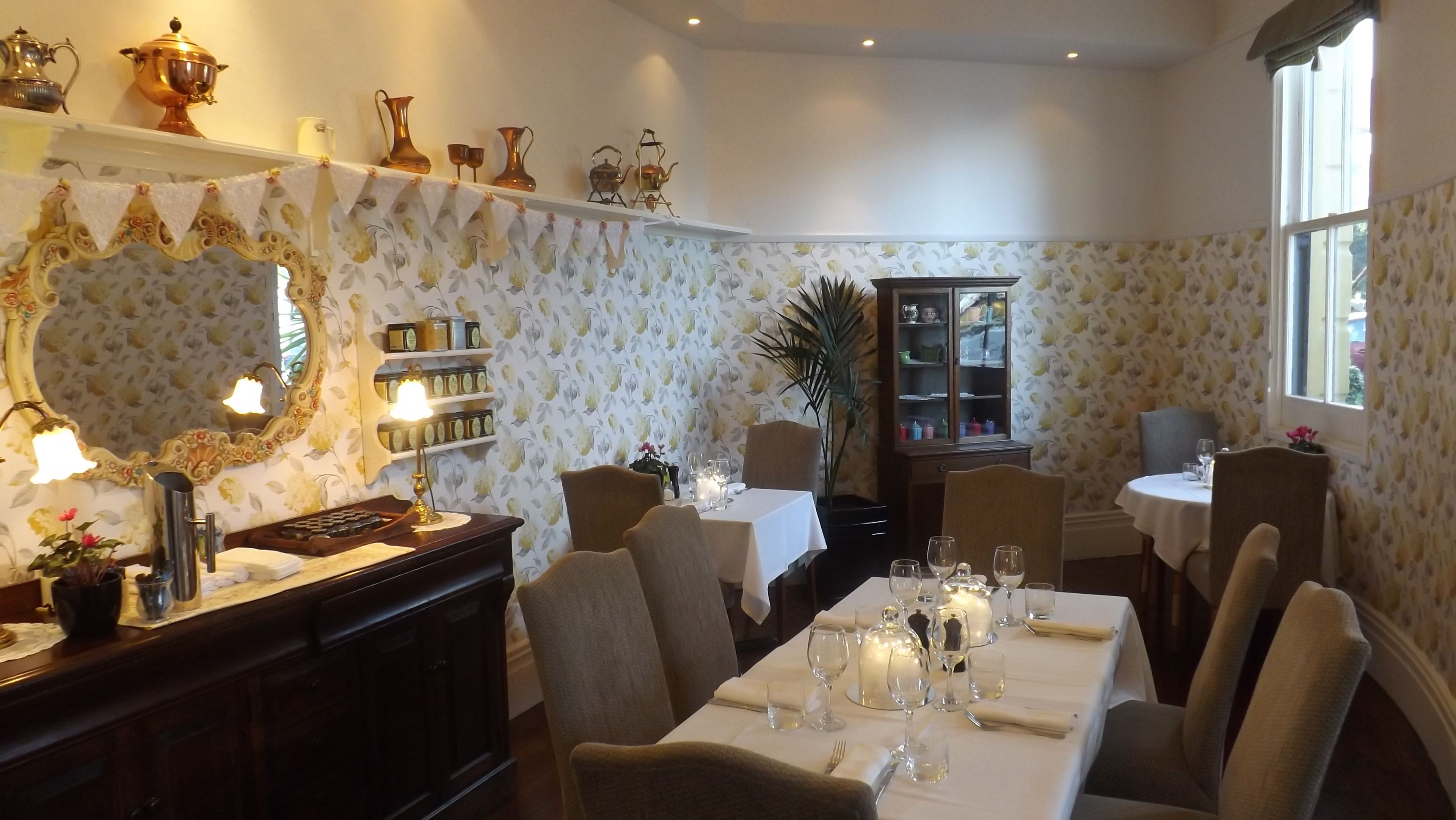 Comedor con una mesa dispuesta para seis comensales, rodeada de sillas, un aparador con cristalería y un espejo con marco decorativo.