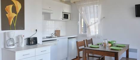 Una cocina moderna con armarios blancos, microondas, cafetera y una mesa de comedor para cuatro personas, con platos verdes.