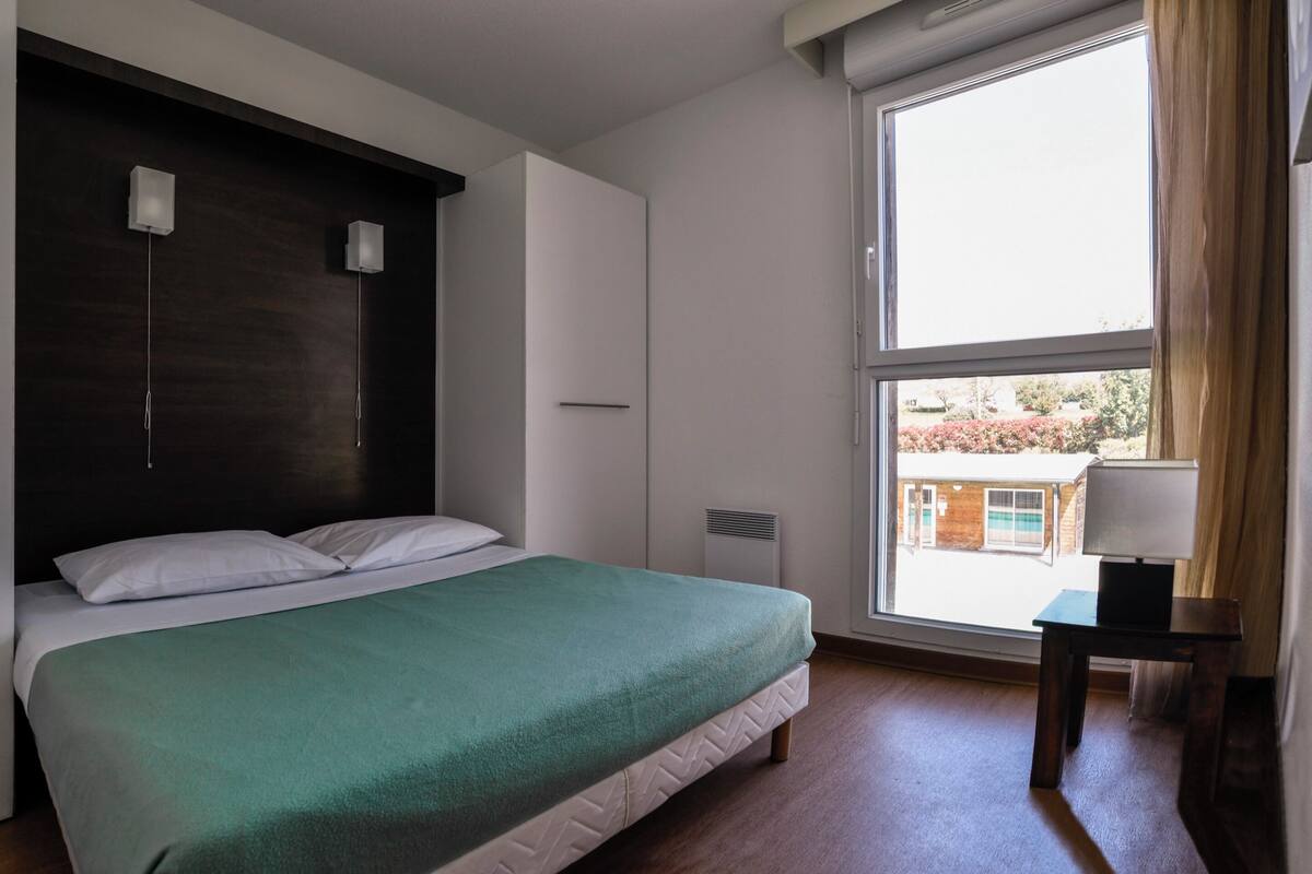 Een slaapkamer met een bed, een raam en een nachtkastje.
