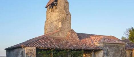 Un edificio histórico de piedra con una torre destacada y tejado de tejas.