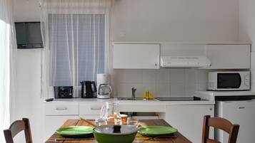 Cocina compacta con armarios blancos, microondas, cafetera y pileta. Hay una mesa de comedor con platos verdes y una jarrón con agua.