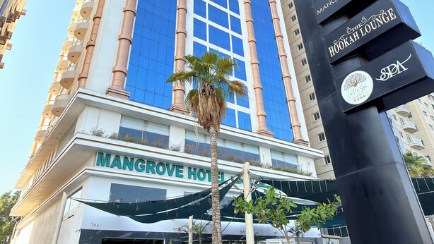 Un hotel alto de fachada azul con un letrero que dice 'Mangrove Hotel'.