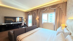 Habitación de hotel con una cama grande, un escritorio con televisor y vistas a edificios a través de la ventana.