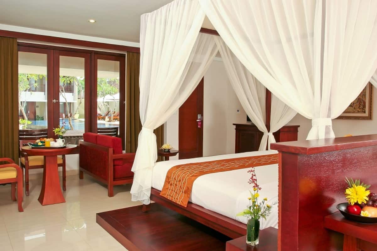 A hotel room with a bed, a sitting area with a table and chairs, a small table with a vase of flowers, and a view of the outside.