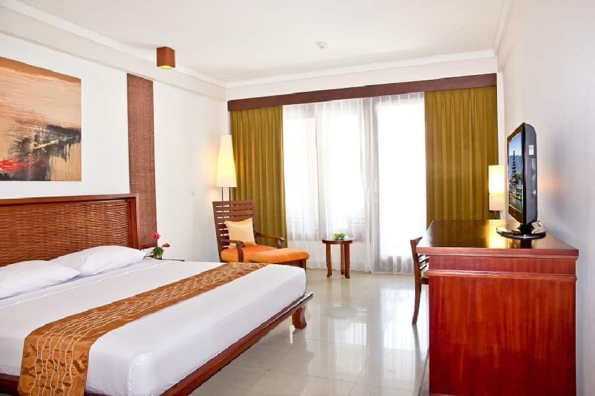 A hotel room with a large bed, a desk, a chair, a television, and a painting on the wall.