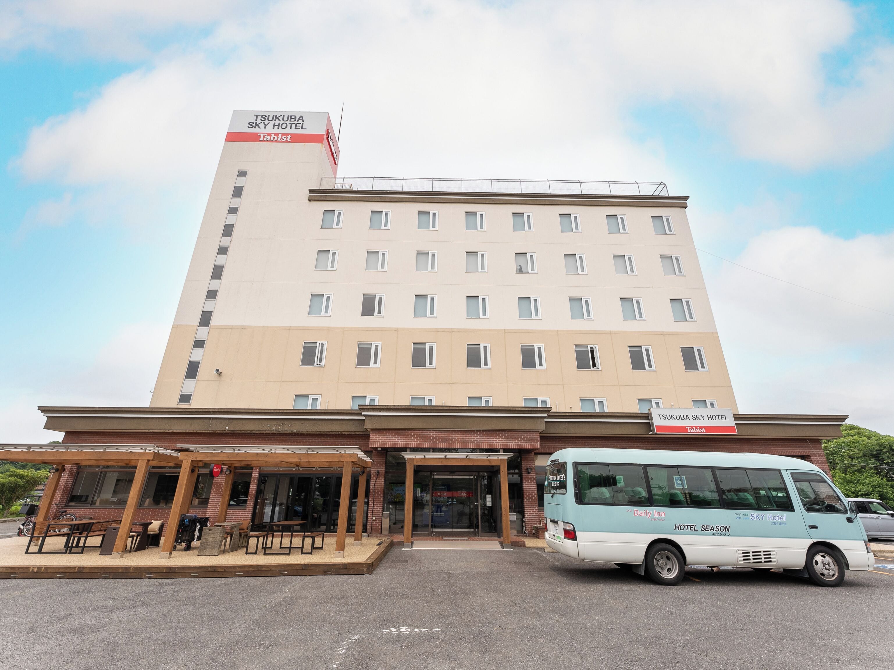 Un hotel de varios pisos con fachada plana, un área de estar al aire libre techada y un autobús lanzadera en la entrada.