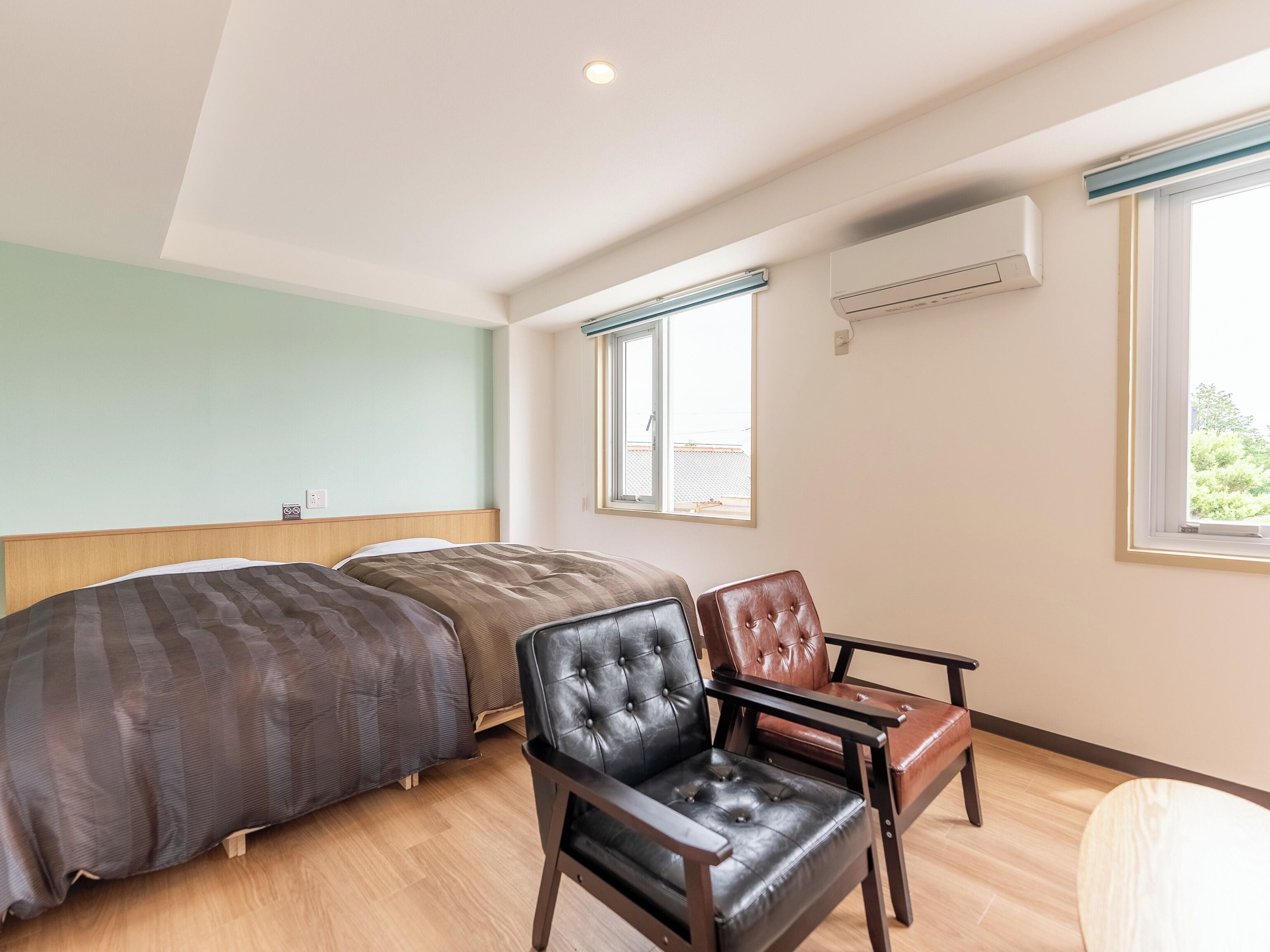 A bedroom with two beds, a chair, a window, and an air conditioning unit.