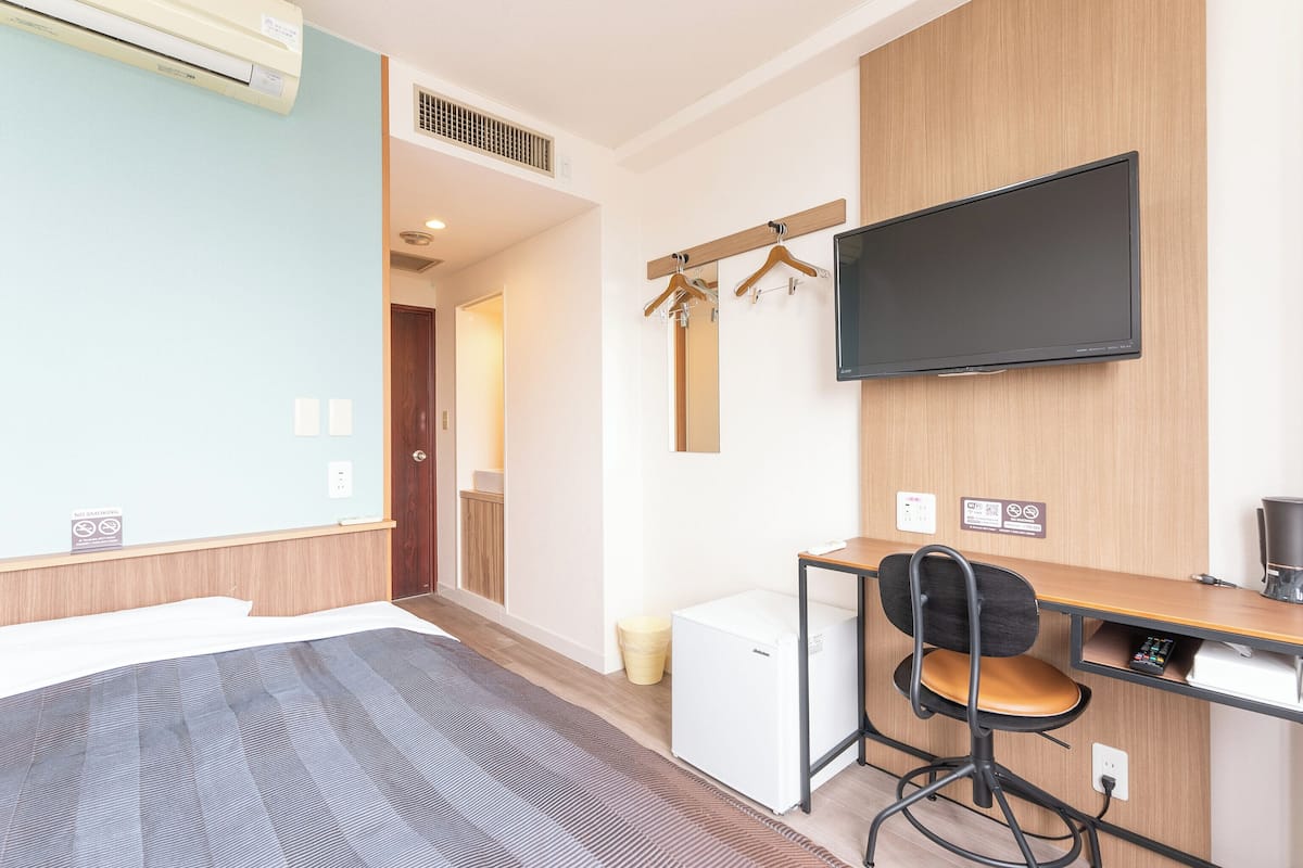 Habitación de hotel con cama, escritorio, silla, televisor, mini refrigerador y armario.