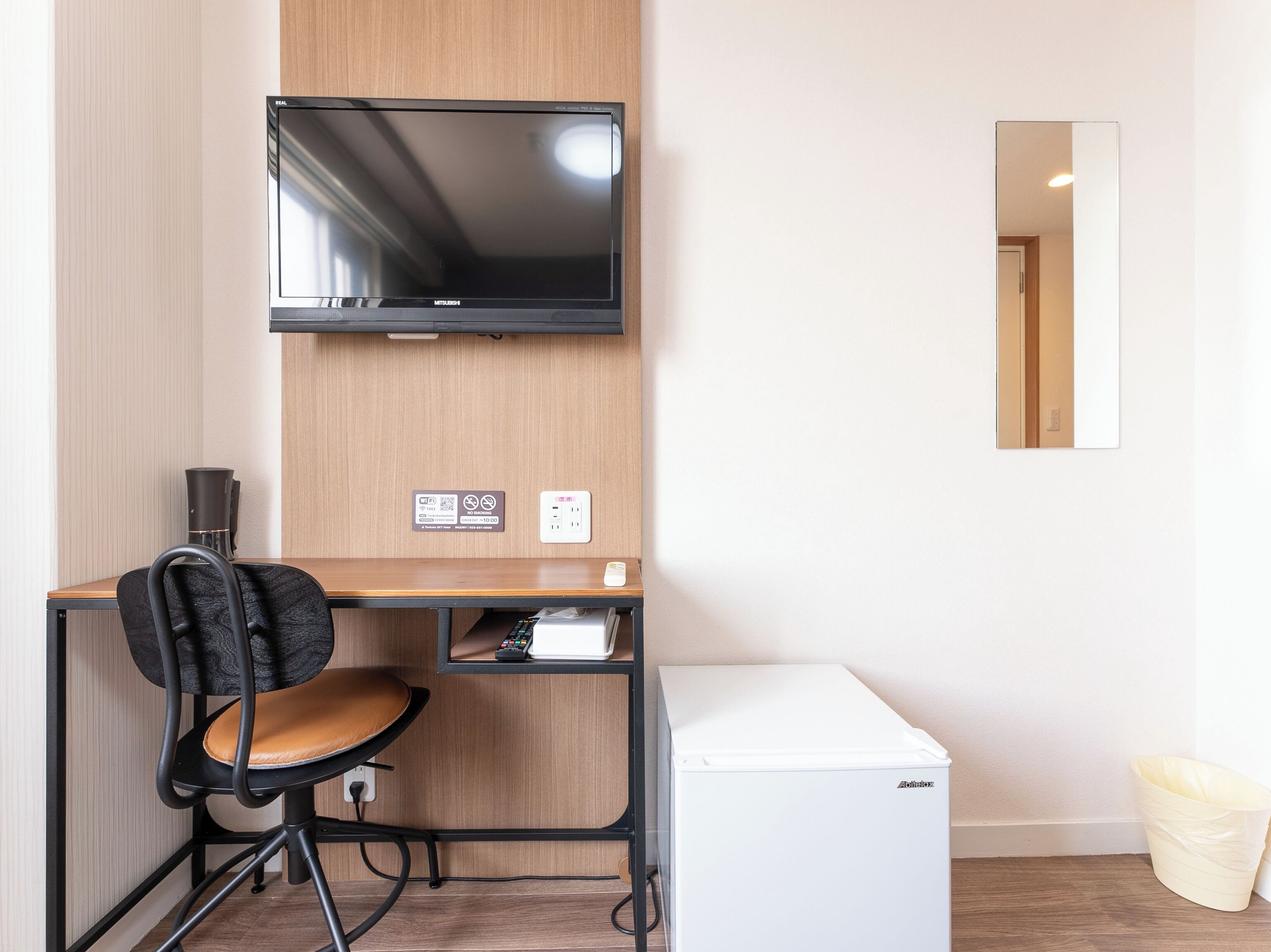 A compact room with a desk, chair, television, and a small refrigerator.
