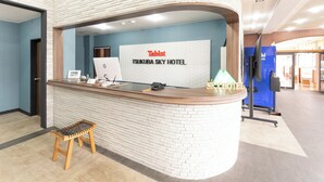 Un comptoir d’accueil à l’hôtel Tsukuba Sky, équipé d’un ordinateur portable, d’un téléphone et d’une petite table.
