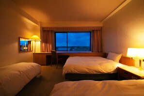 A hotel room with two beds, a desk, and a chair. There is a window with curtains and a view of the cityscape. - Mito Hotel Season (Mito)
