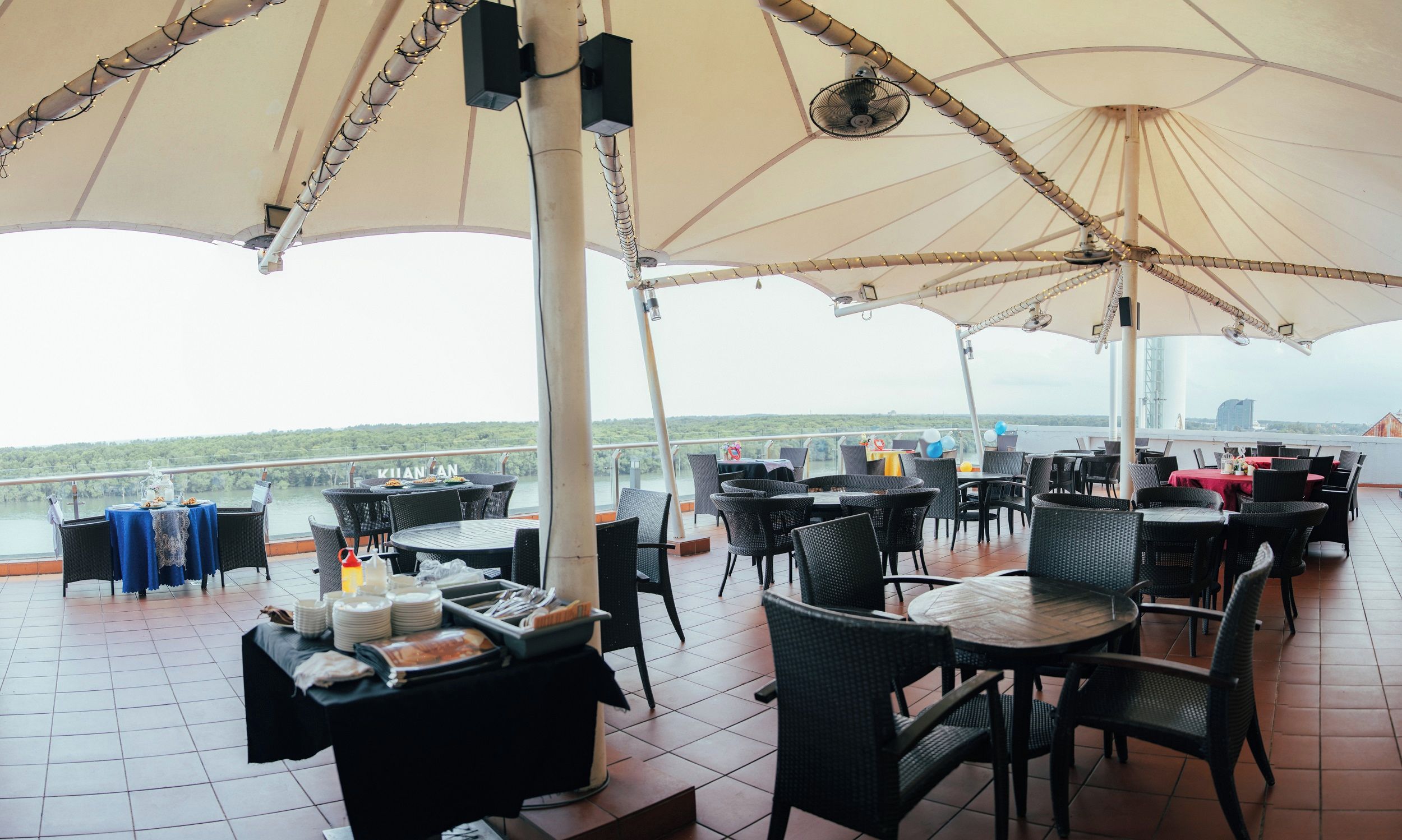 An outdoor dining area with tables and chairs, umbrellas, and a view of the water.