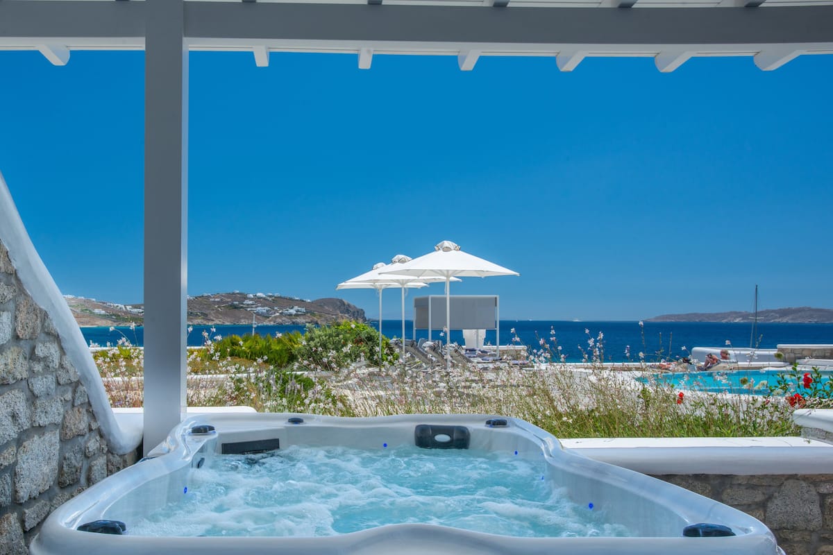 A hot tub with a view of the sea and a pool area.