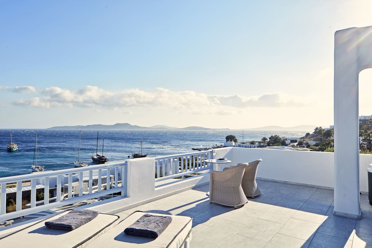 A terrace with white railings, lounge chairs, and a view of the sea and distant mountains.