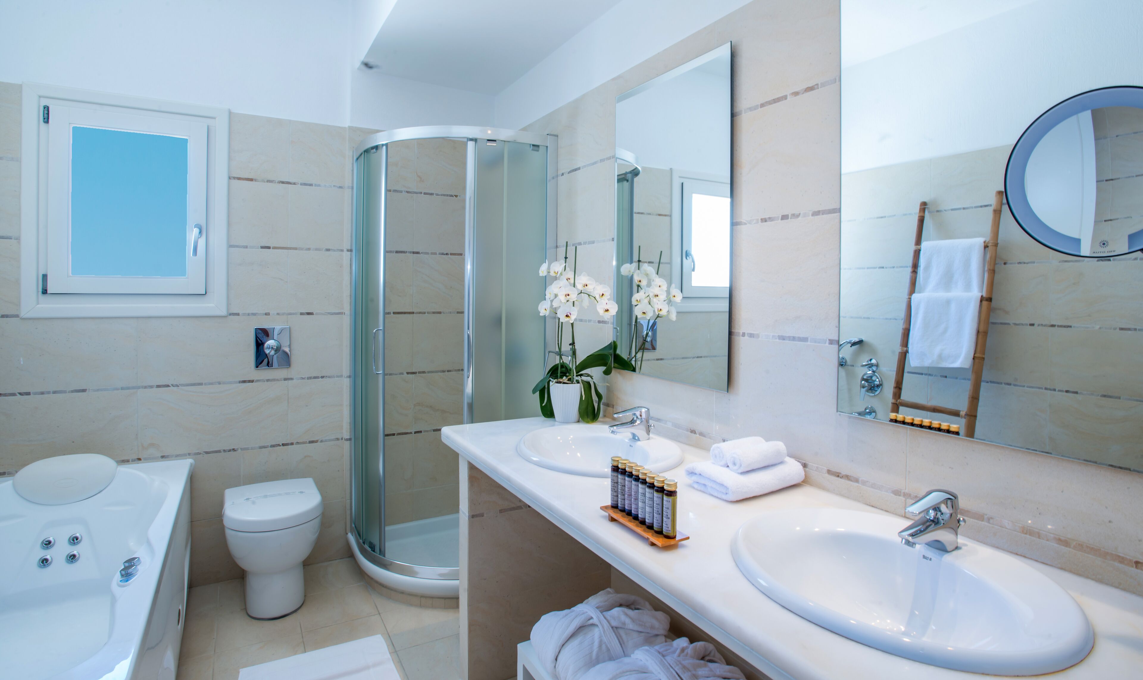 Un baño moderno con ducha de vidrio, dos lavamanos, un inodoro y un espejo grande.
