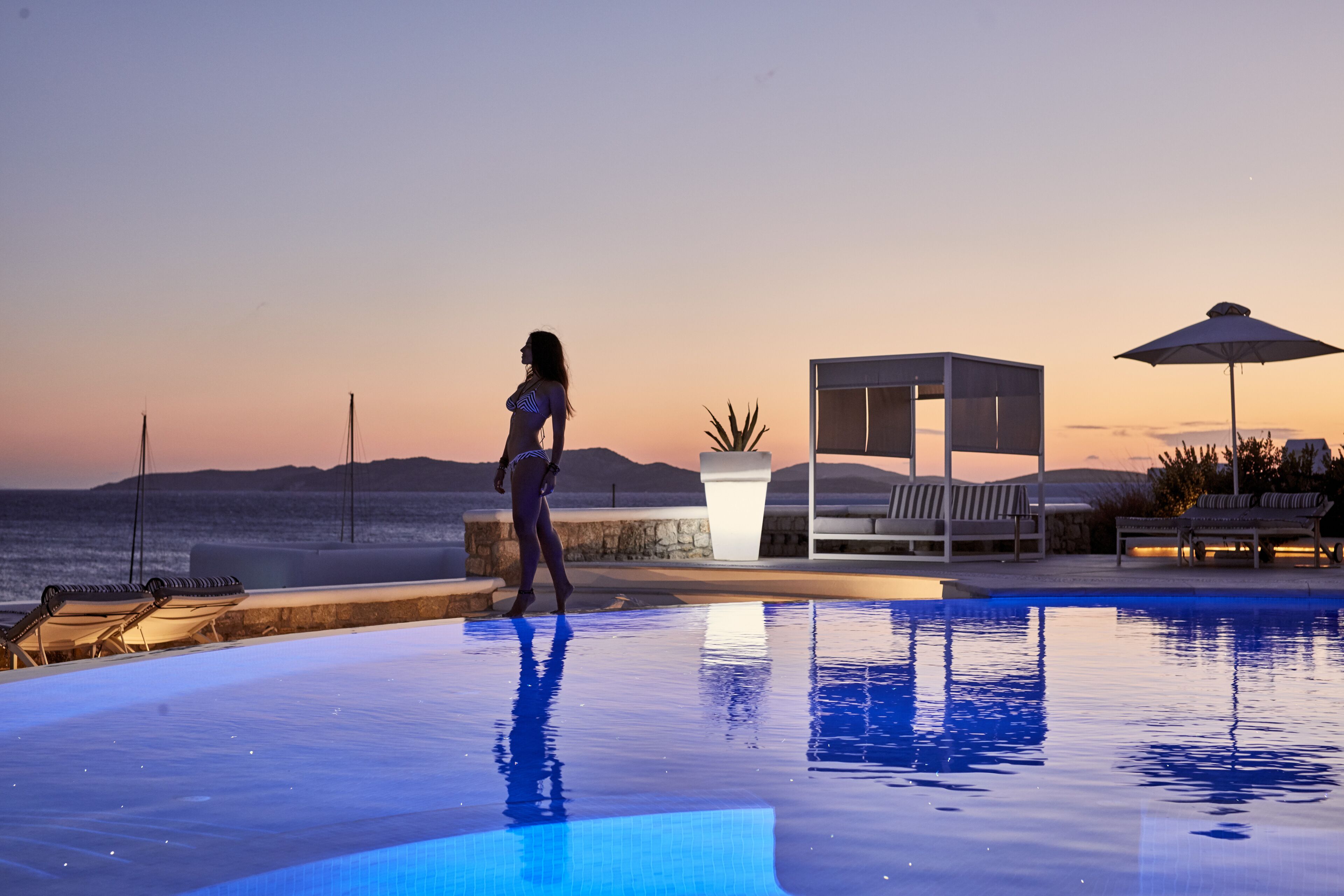 Mulher ao lado de uma piscina com vista para o pôr do sol.