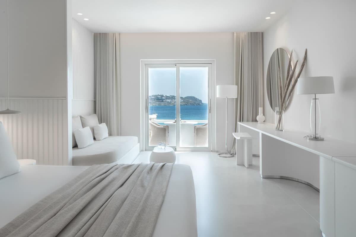 A modern hotel room with a large bed, a seating area with a view of the sea, and a balcony.