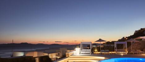 A pool area with lounge chairs and umbrellas, overlooking a scenic ocean view at dusk.