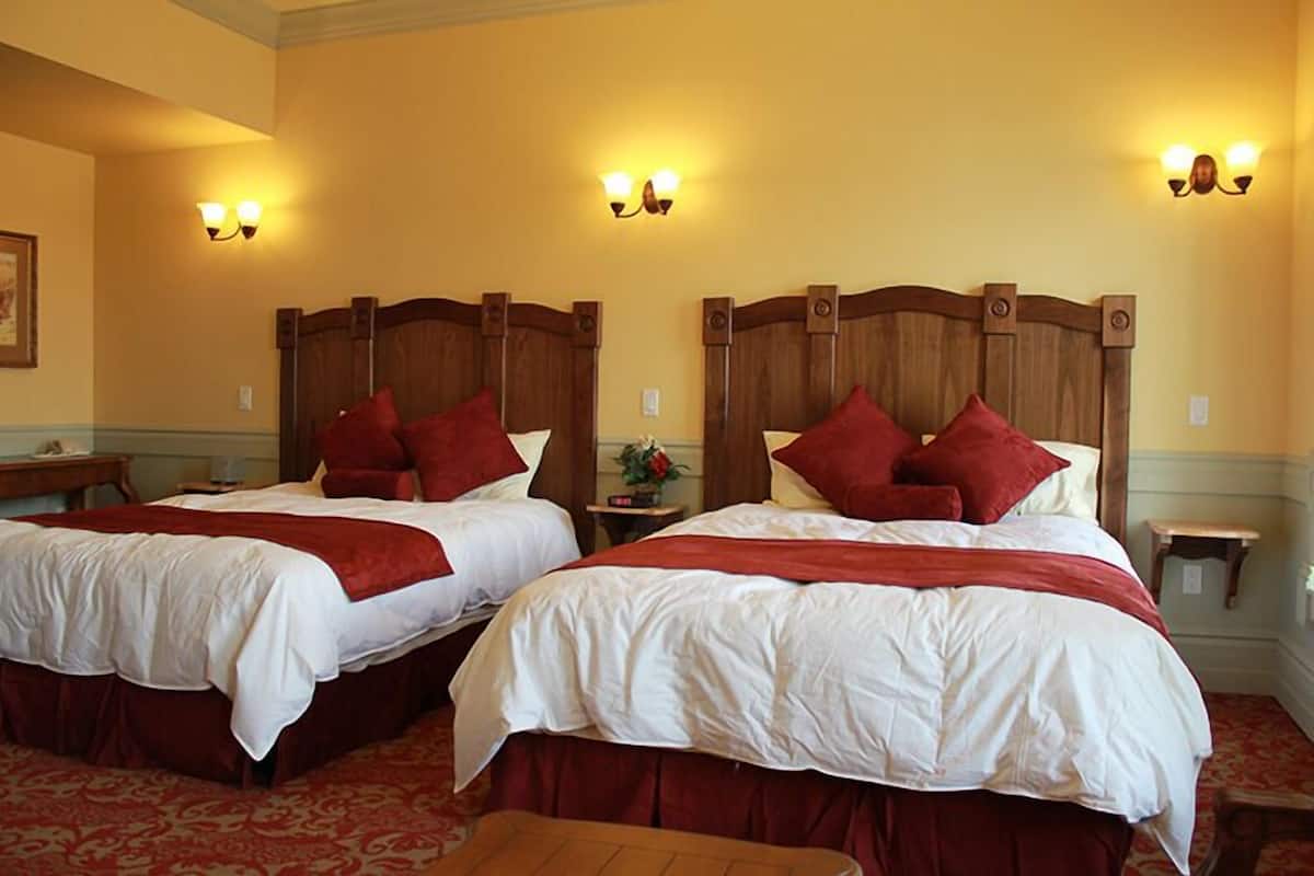 Two double beds with wooden headboards, red pillows, and white bedding in a hotel room.