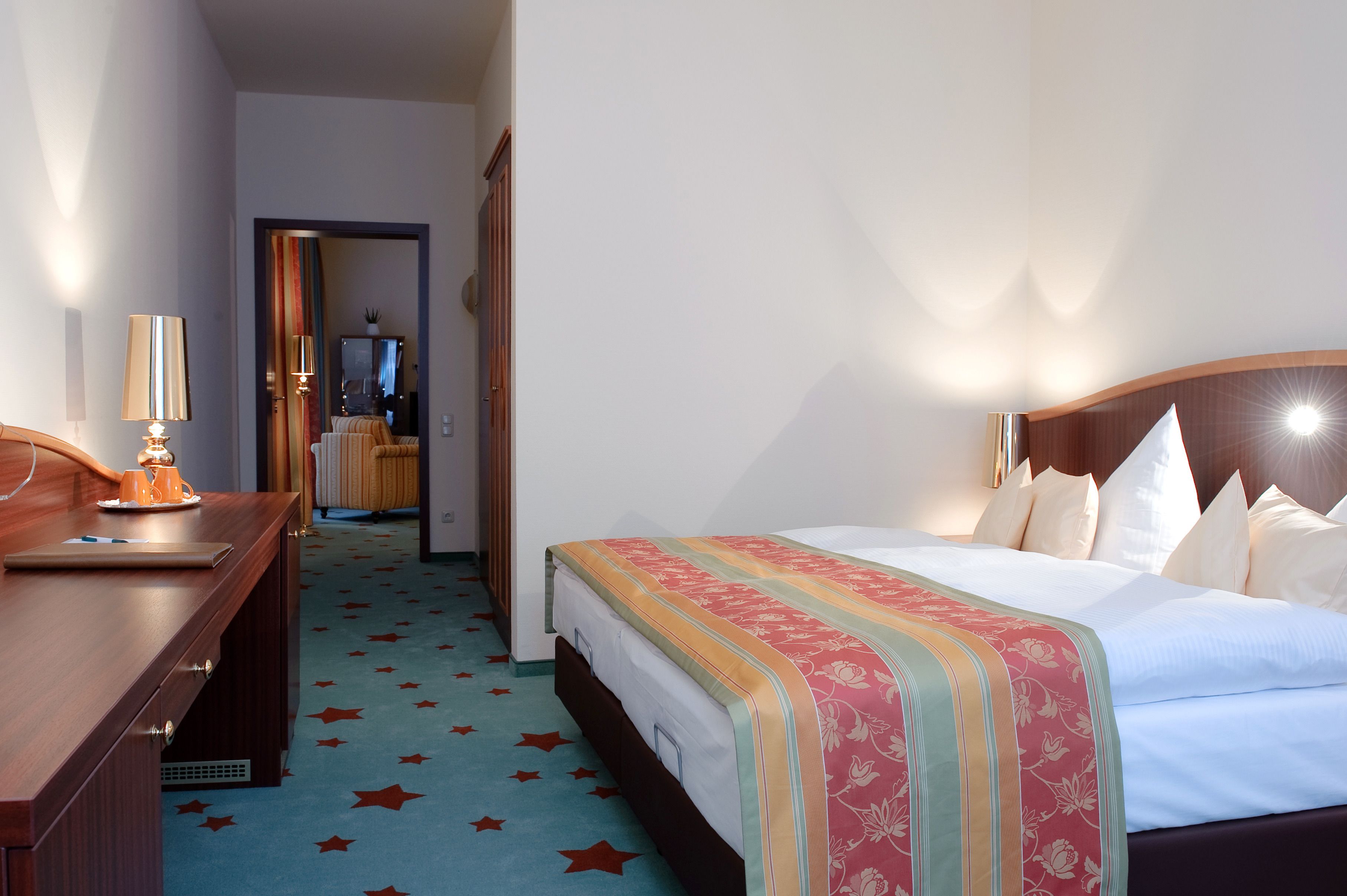 Ein Hotelzimmer mit Bett, Nachttisch, Lampe und einem teppichartigen Boden mit Sternenmuster.