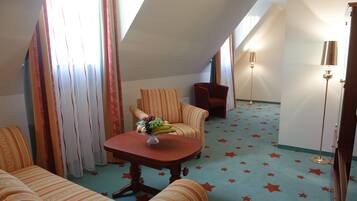 Une chambre d’hôtel avec une moquette à motifs étoilés, des meubles rembourrés à rayures et une table sur laquelle se trouve un panier de fruits.