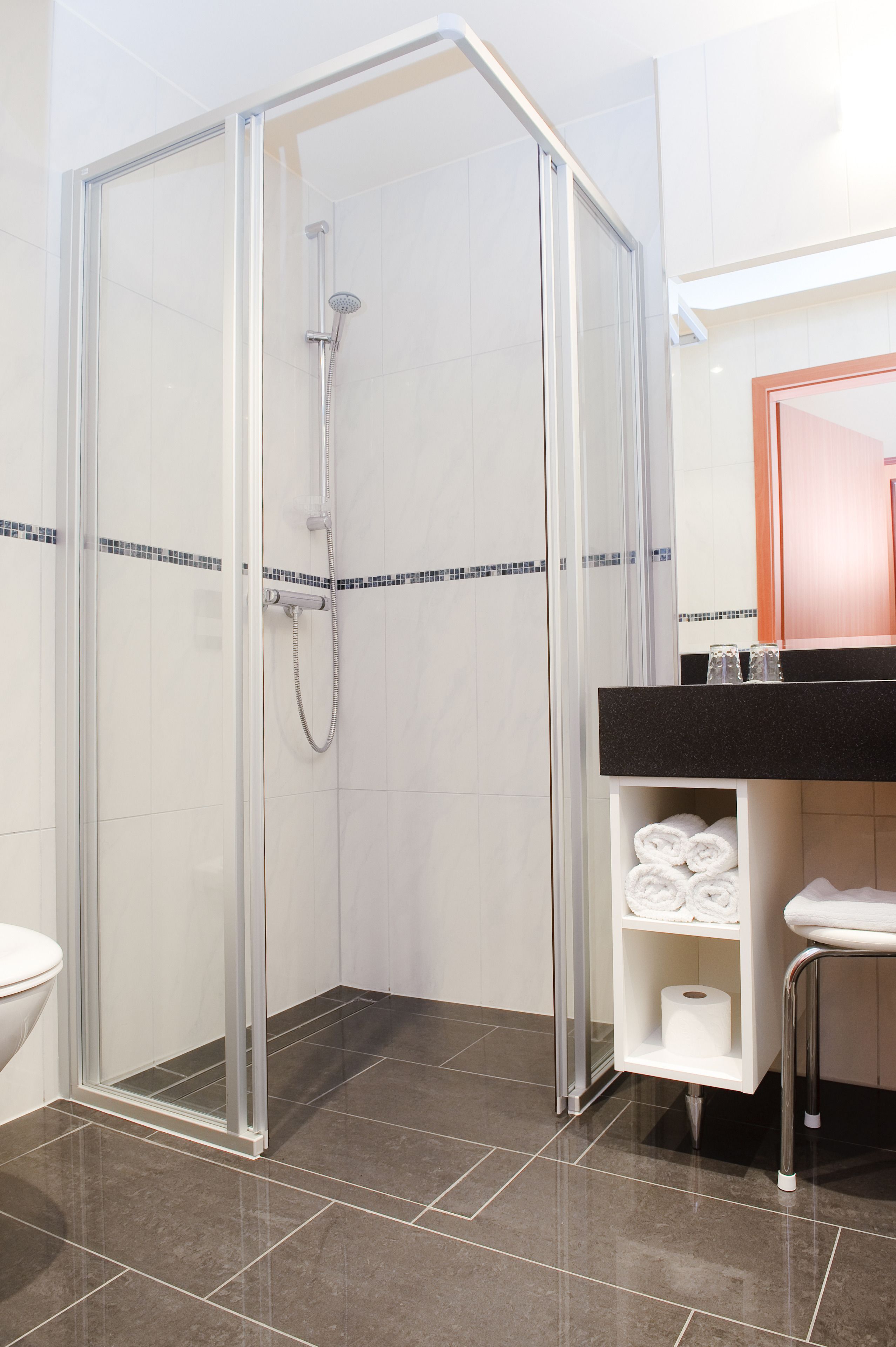 Een moderne badkamer met een douchecabine van glas, een zwarte wastafel en een witte wasbak.