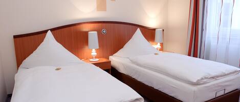 A hotel room with two single beds, each with a wooden headboard, white bedding, and bedside lamps.