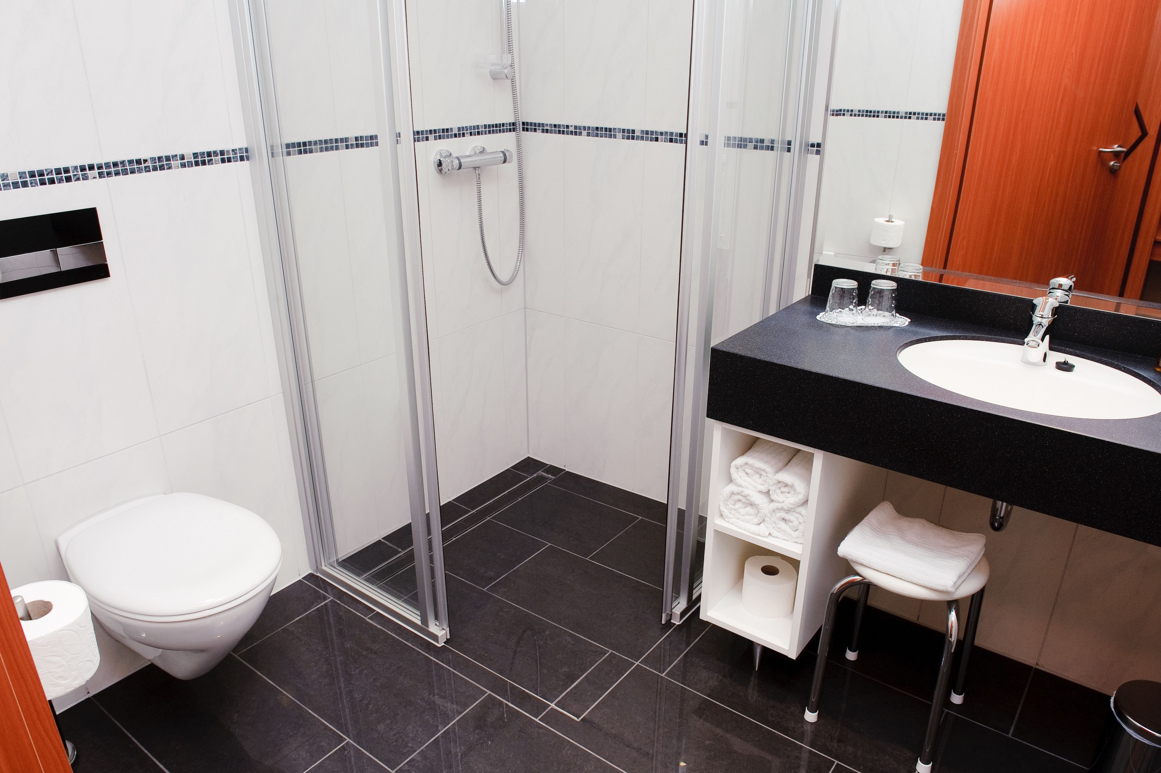 Ein modernes Badezimmer mit Duschkabine aus Glas, einer weißen Toilette und einem schwarzen Waschtisch mit Spiegel.