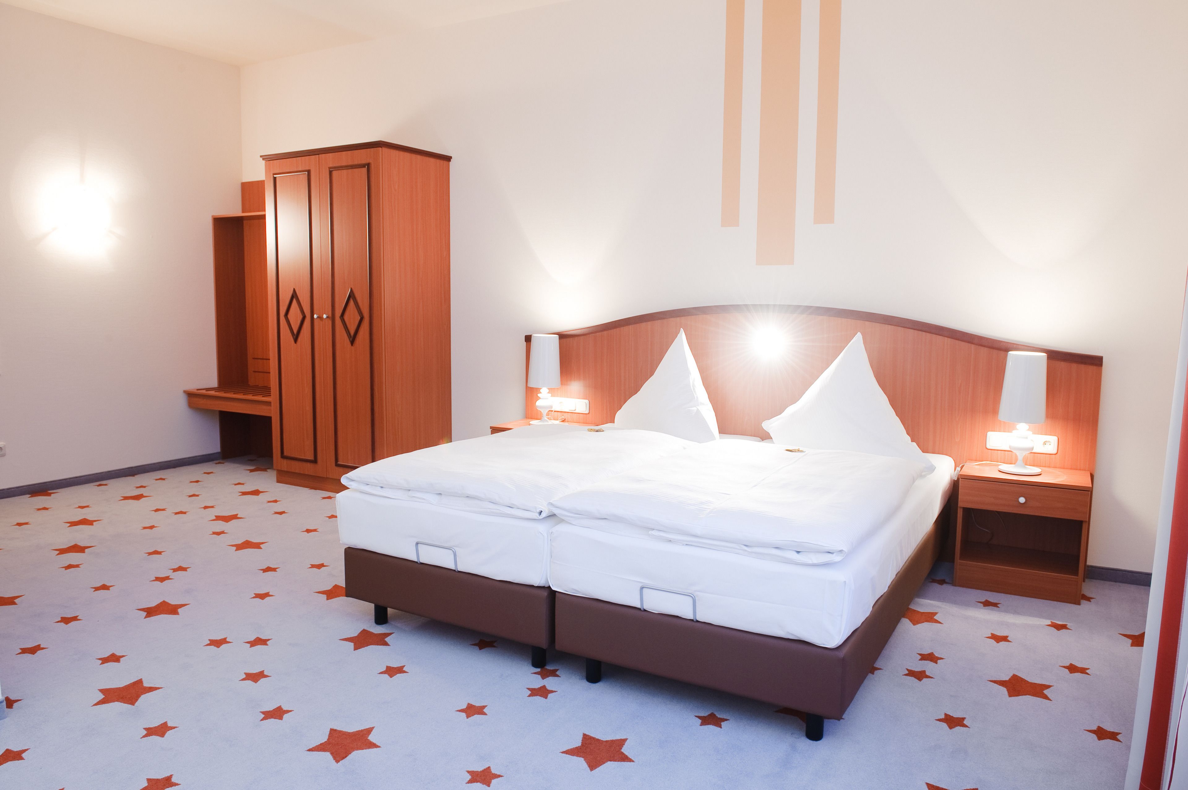 A hotel room with a bed, nightstands, a wardrobe, and a star-patterned carpet.
