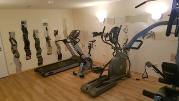 A gym with various exercise equipment, including treadmills and stationary bikes, arranged in a spacious room with wooden flooring.