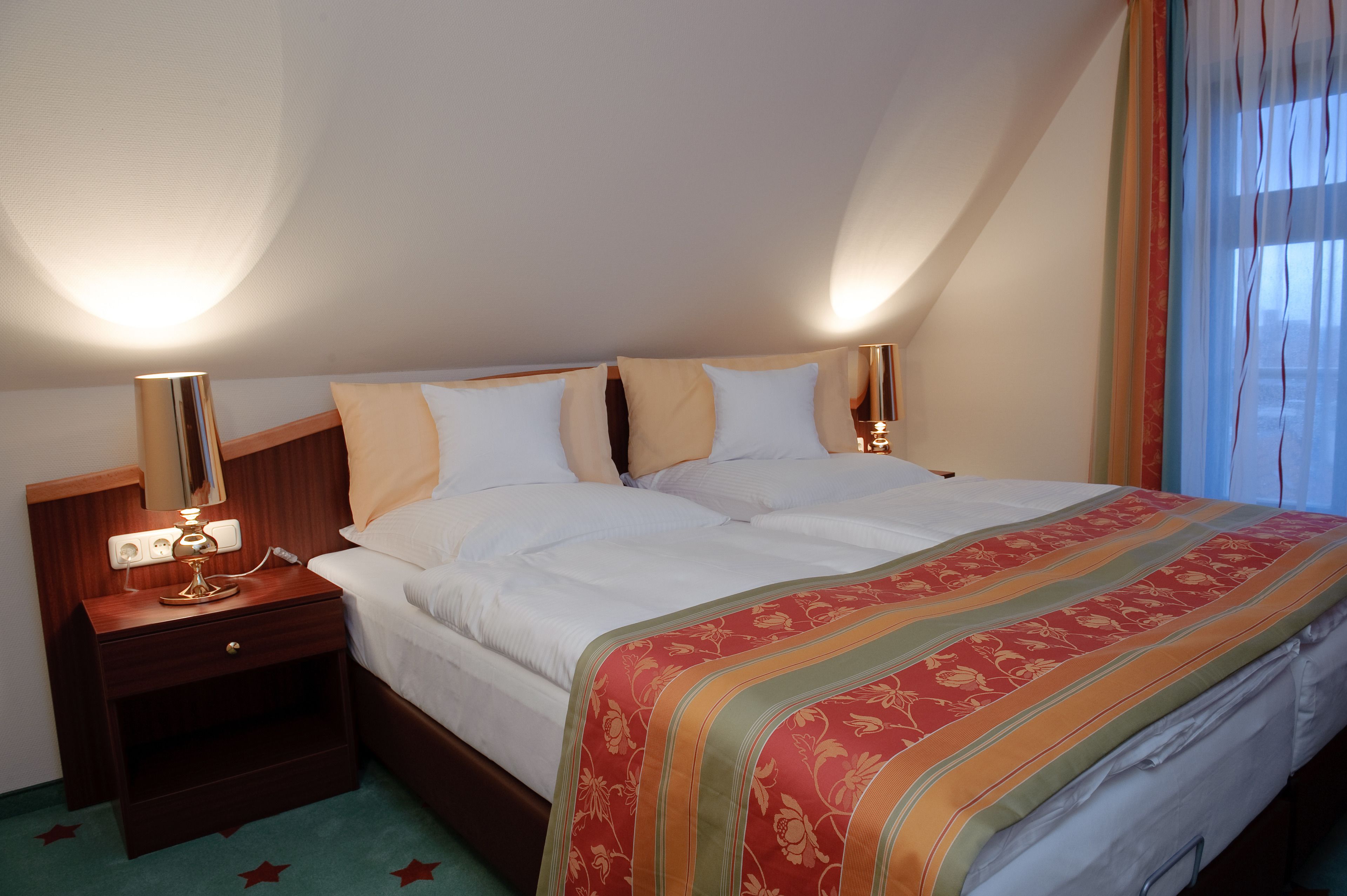 A hotel room with a bed, bedside tables, and a lamp.