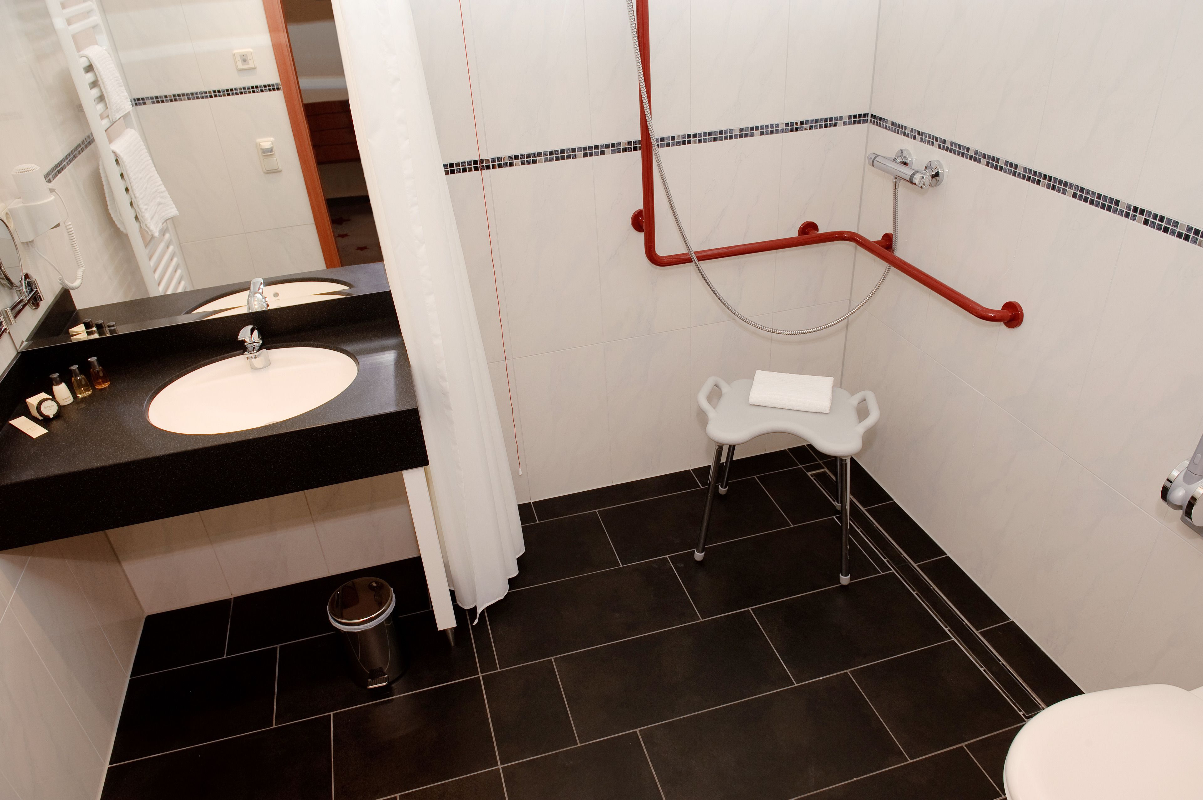 A bathroom with a black countertop sink, a white toilet, and a shower area with a red grab bar.