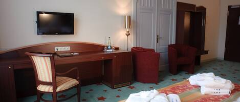 Une chambre d’hôtel équipée d’un bureau, d’une télévision, d’une chaise, d’une armoire et d’un lit avec des serviettes.