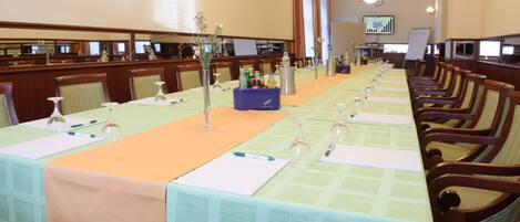 A conference room with long tables, chairs, and a projector screen.