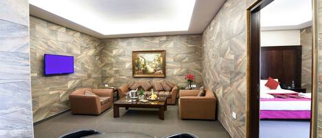 A modern living room with a stone wall, a flat-screen TV, a painting, a sofa set, and a dining area with a table and chairs.