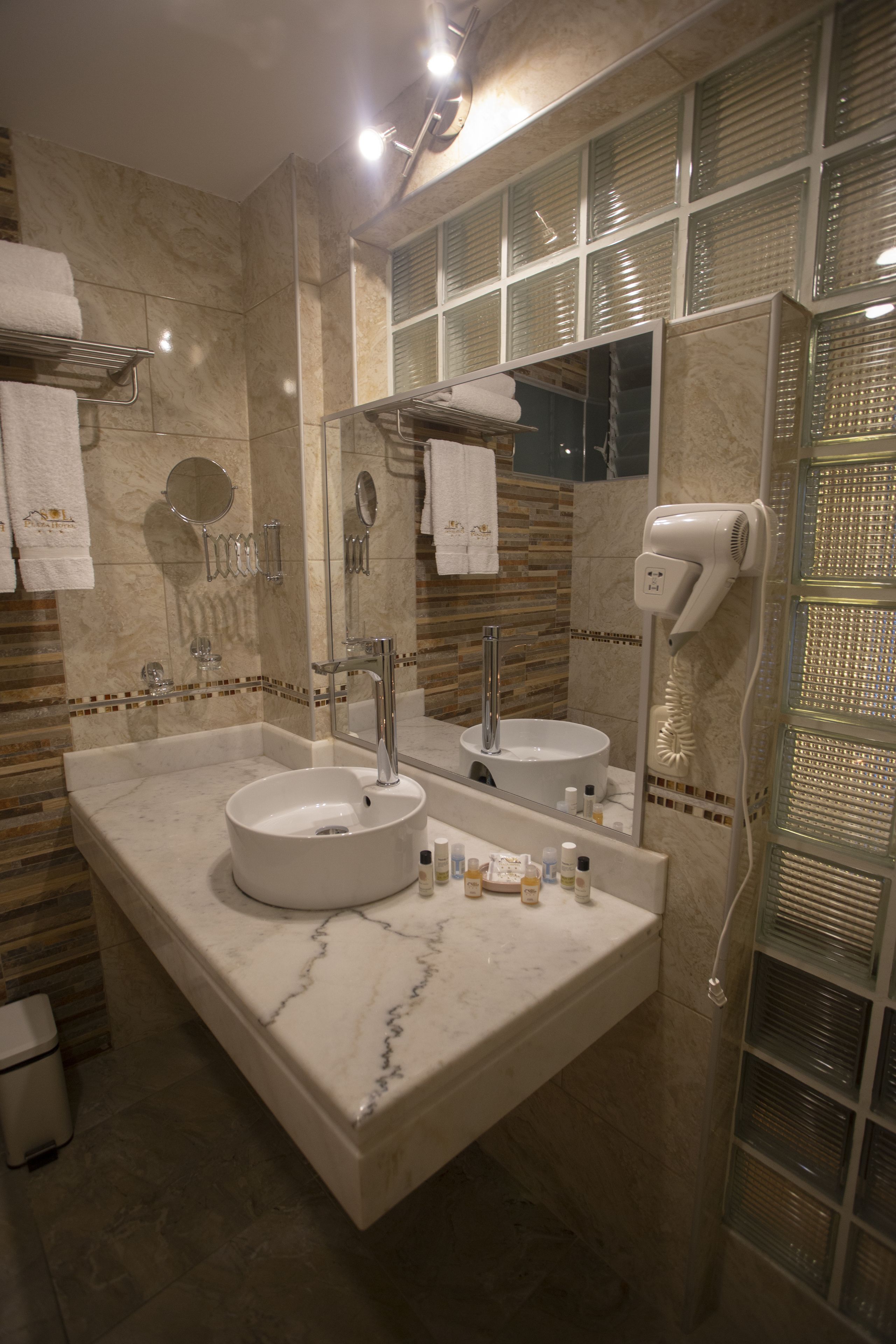 A bathroom with a marble vanity, two sinks, a hairdryer, and a mirror.