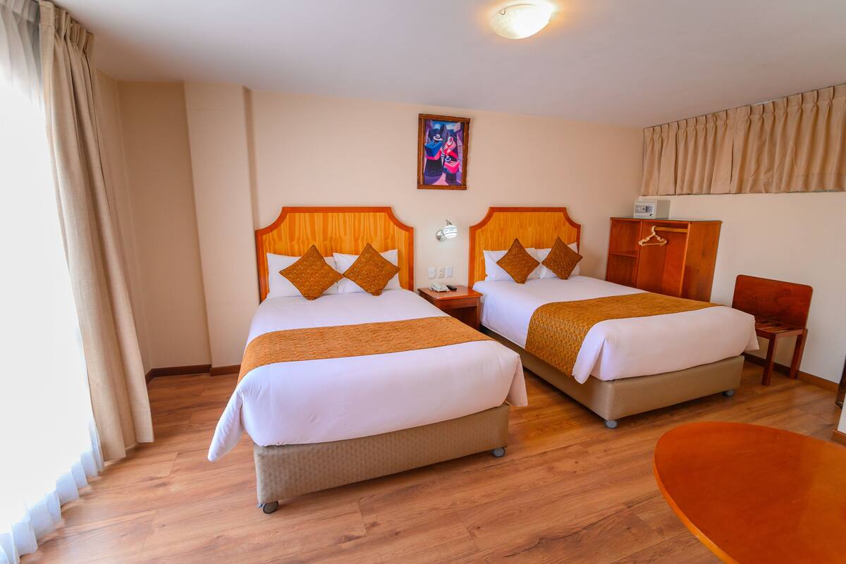 Una habitación de hotel con dos camas, suelo de madera, un cuadro en la pared y una mesita.