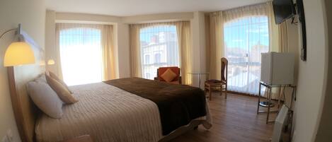 Habitación de hotel con una cama grande, un escritorio, una silla, un televisor y un balcón con vistas.
