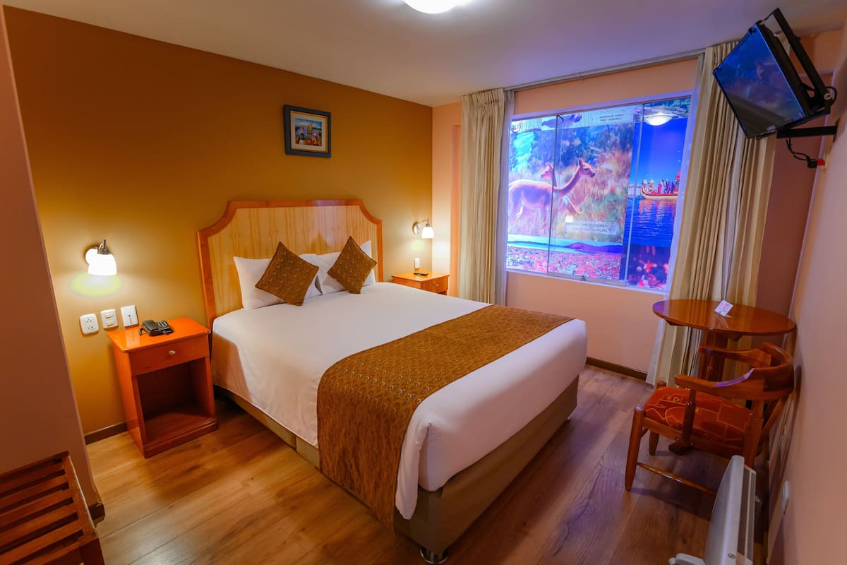 A hotel room with a large bed, bedside lamps, a television, and a window with curtains.