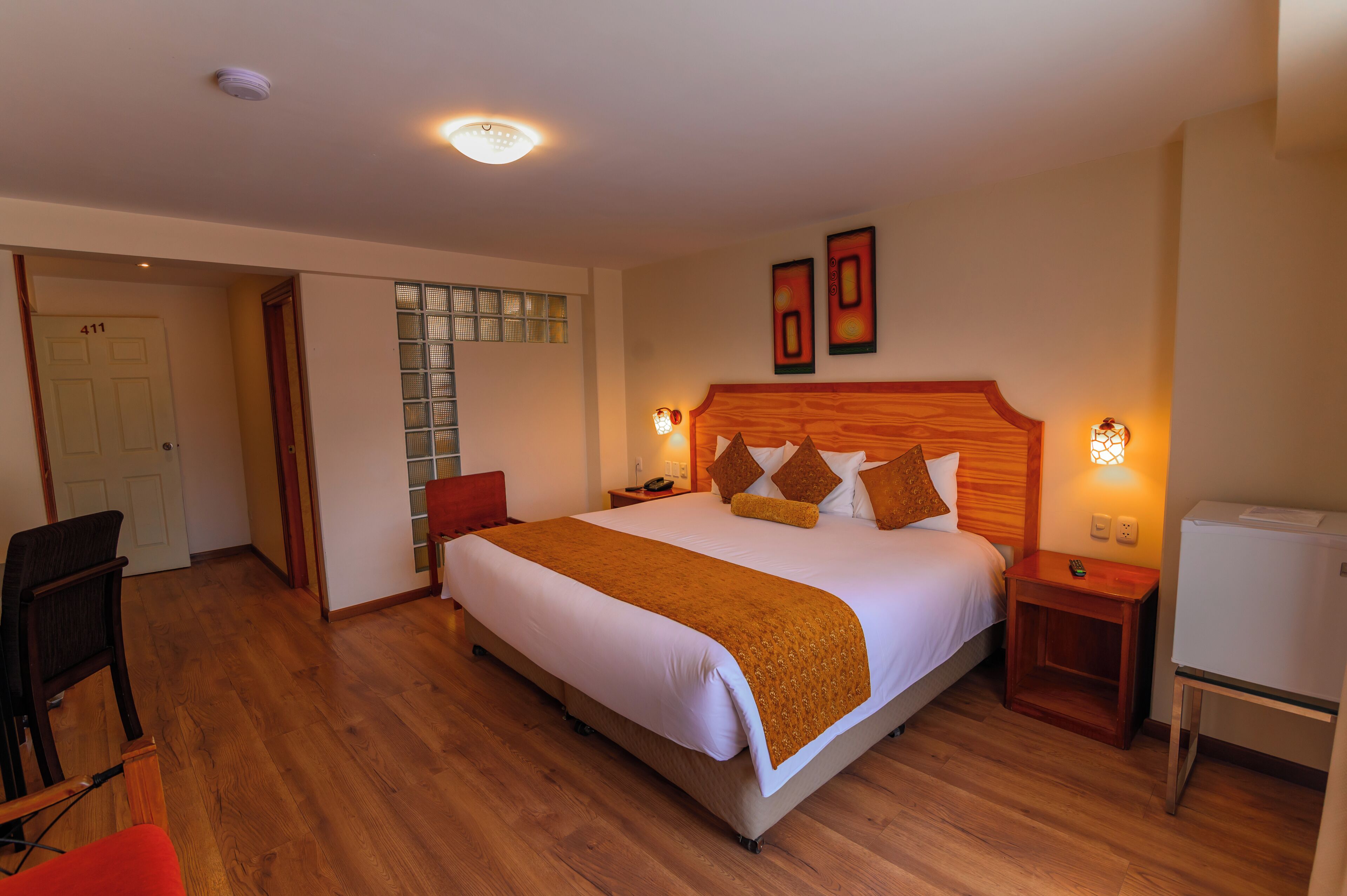 A hotel room with a large bed, wooden headboard, bedside tables, a desk, and a chair.