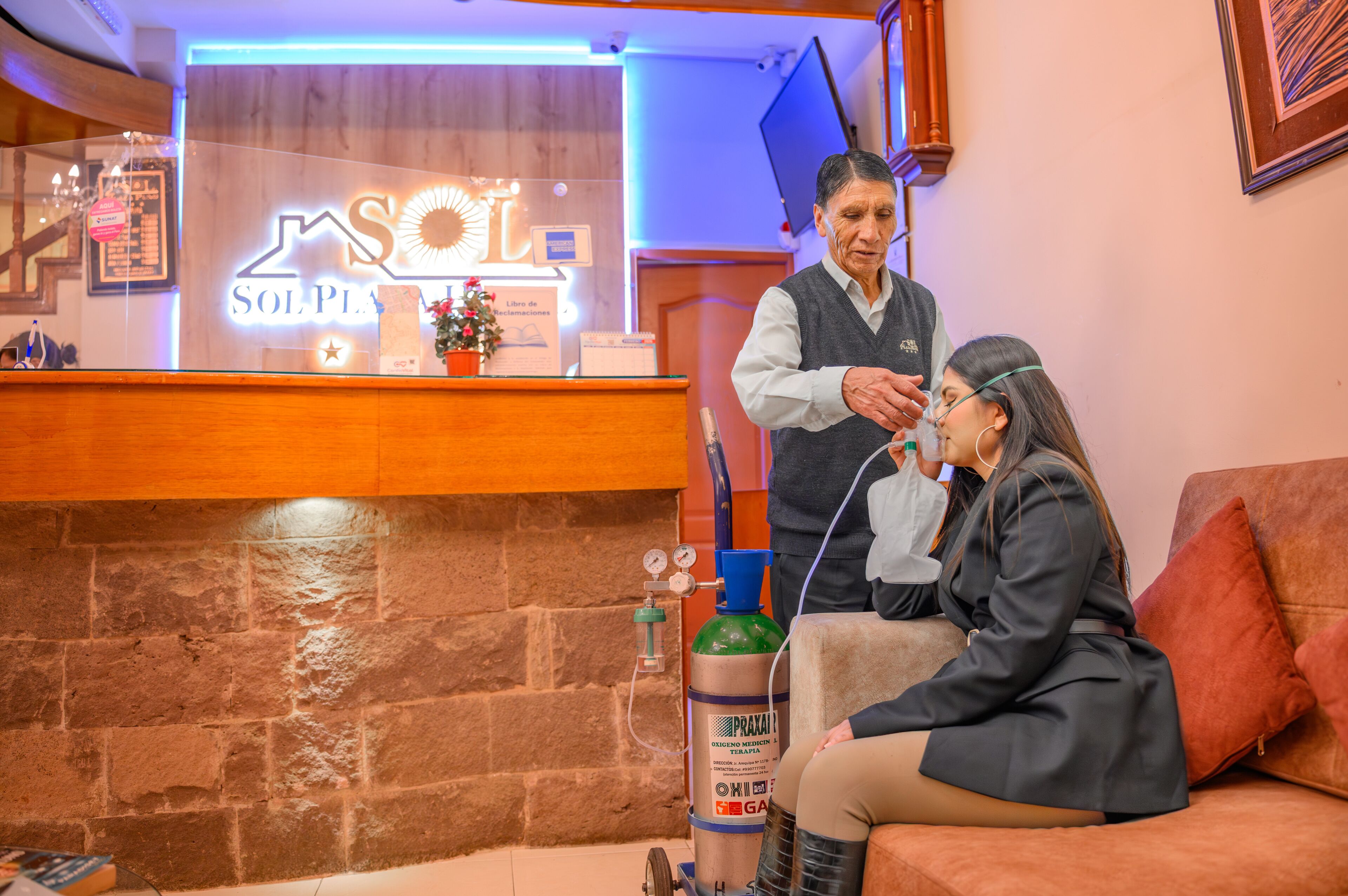 A reception area with a wooden counter, a reception desk, a wall-mounted TV, and a gas cylinder.